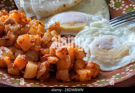 Sur des œufs moyens avec des pommes de terre et chorizo ou huevos estrellados con papas y chorizo, sur une plaque de boue ou d'argile mexicaine dans le cadre d'un petit déjeuner mexicain. Banque D'Images