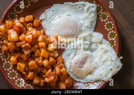 Sur les œufs moyens avec pommes de terre et chorizo sur le côté sur une plaque d'argile ou de boue mexicaine sur une table en bois dans le cadre d'un petit déjeuner mexicain complet. Banque D'Images