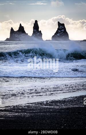 Les vagues s'écrasent sur la plage en face des piles de basalte Reynisdrangar en hiver à Vík í Mýrdal sur la côte sud de l'Islande Banque D'Images