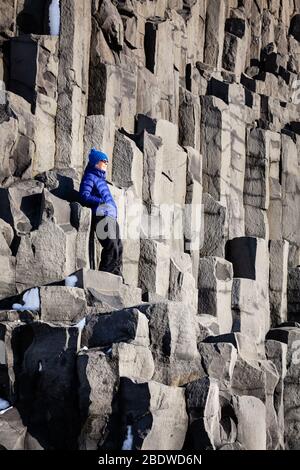 Une femme debout sur des colonnes de basalte à Reynisfjara plage de sable noir en hiver près de Vík í Mýrdal, au sud de l'Islande Banque D'Images