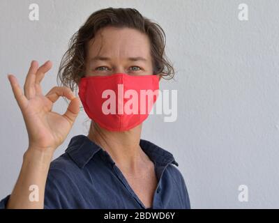 La femme caucasienne porte un masque de visage fait maison et donne le signe OK pendant la pandémie du corona-virus 2019-20. Banque D'Images