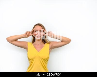 Portrait d'une jeune femme qui fait des signes de main sur ses yeux et souriant. Banque D'Images