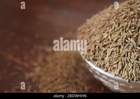 Graines de Cumin séchées dans un bol argent sur la vieille table en bois. Style rustique Banque D'Images