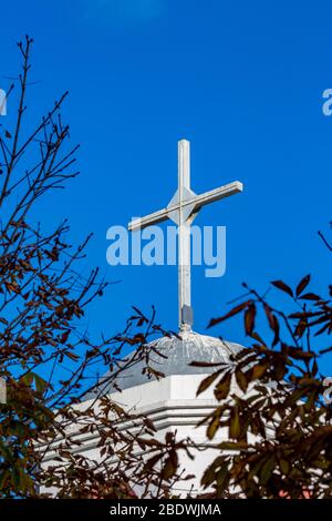 La croix blanche de l'église orthodoxe du village de Fanari, région de Xanthi, Grèce du Nord, clocher vue partielle contre ciel bleu clair, encadré par des branches de châtaigniers Banque D'Images