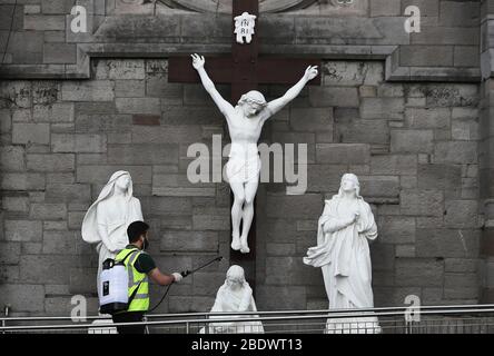 Un homme vaporise du désinfectant sur une statue de la crucifixion de Jésus à l'extérieur de l'église Sainte Marie des Anges à Dublin, vendredi Saint, les vacances chrétiennes commémorant la crucifixion de Jésus et sa mort à Calvary. Banque D'Images