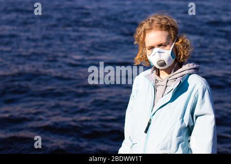 Fille dans le masque médical pour la protection respiratoire regardant dans l'appareil photo. L'adolescent féminin porte un respirateur. Copier l'espace sur fond avec de l'eau Banque D'Images