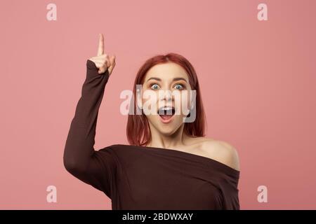 Femme au gingembre surprise avec main levée isolée sur fond rose vide en studio. Banque D'Images