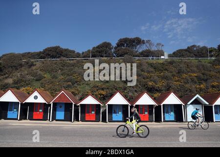 Les cyclistes font leur chemin devant des cabanes de plage vacantes sur le front de mer de la plage de Bournemouth, tandis que le Royaume-Uni continue de se maintenir en place pour aider à freiner la propagation du coronavirus. Banque D'Images