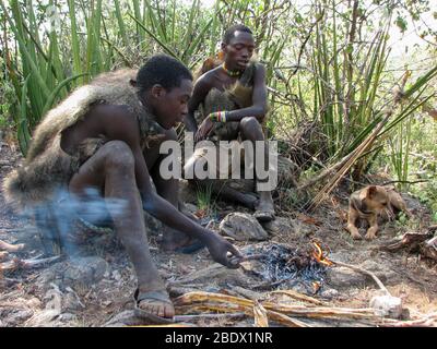 Les tribébins d'Hadzabe assis autour d'un feu de camp de cuisson de viande photographiée au lac Eyasi, Tanzanie Banque D'Images