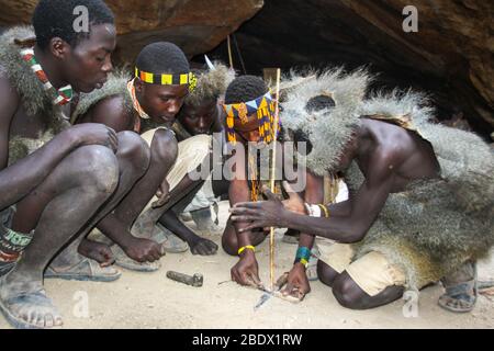 Les tribébins d'Hadzabe assis autour d'un feu de camp de cuisson de viande photographiée au lac Eyasi, Tanzanie Banque D'Images