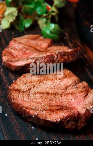 Des portions épaisses de steak de filet frit sont servies, saupoudrées de sel, sur une vieille planche en bois. Le plat est prêt à servir. Banque D'Images