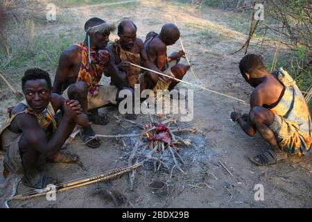 Les tribébins d'Hadzabe assis autour d'un feu de camp de cuisson de viande photographiée au lac Eyasi, Tanzanie Banque D'Images