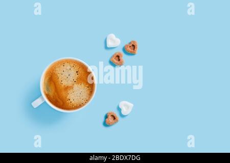 Tasse de café fort du matin avec cinq morceaux de sucre en forme de coeur sur fond bleu. Banque D'Images