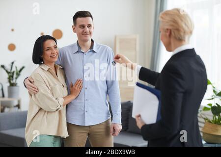 Un jeune couple heureux achetant la nouvelle maison ils prennent les clés de leur nouvelle maison tout en se tenant dans la chambre avec le realtor Banque D'Images
