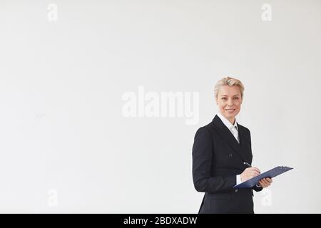 Portrait d'une femme d'affaires mûre réussie en costume noir signant un contrat et souriant à l'appareil photo isolé sur fond blanc Banque D'Images