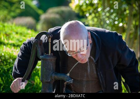 Homme boit d'une pompe à eau dans un parc. Close up portrait contre green bokeh background. Banque D'Images