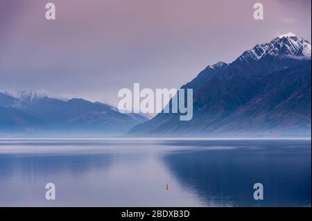 Coucher du soleil sur le lac Hawea tranquille, en Nouvelle-Zélande. Mist plane sur les montagnes avec le lac toujours en premier plan Banque D'Images