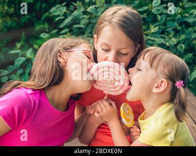 Trois petites filles drôles dans des tee-shirts colorés léchant de grandes sucettes - sur la terrasse du jardin Banque D'Images