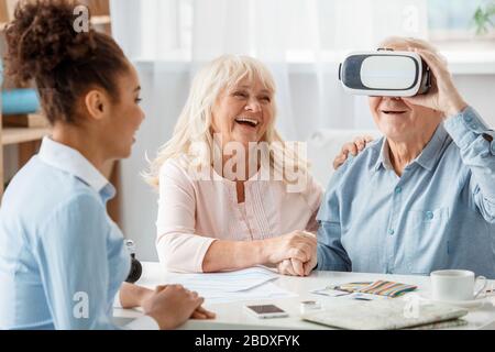 Agent de voyage au bureau avec des clients seniors homme portant un casque de réalité virtuelle riant gai Banque D'Images