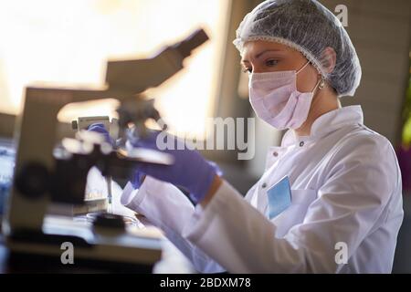 Une travailleuse de laboratoire féminine regarde un échantillon de sang au microscope Banque D'Images