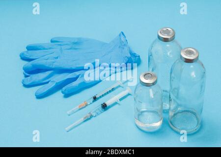 Gants en latex bleu, bouteilles en verre pour la médecine liquide et seringues à injecter sur fond bleu. Vue de dessus. Concept de santé et de médecine. Banque D'Images