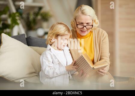 Grand-mère dans des lunettes lecture d'un livre à son fils pendant leur temps de loisirs à la maison Banque D'Images