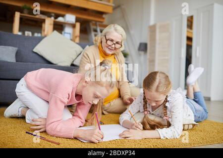 Deux petites filles qui mentent sur le sol et qui s'étirent avec leur grand-mère en arrière-plan, elles sont à la maison Banque D'Images