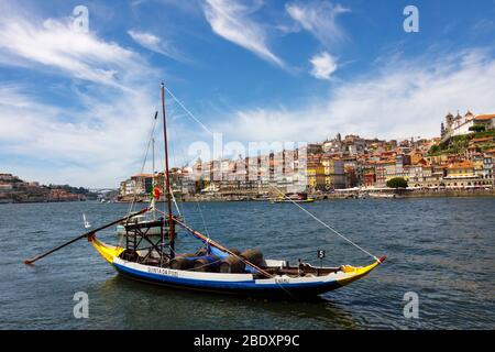 Porto, Portugal : un bateau traditionnel chargé de fûts de vin est amarré sur le fleuve Douro en face de la vieille ville de la rive. Banque D'Images