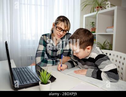 Enfant faisant des devoirs avec sa mère. Famille à la maison. Apprentissage à la maison, apprentissage en ligne, concept d'auto-quarantaine Banque D'Images