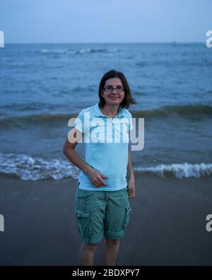 Belle bonne jeune femme caucasienne dans un t-shirt bleu sur la plage pendant le lever du soleil. Concept de voyage Banque D'Images