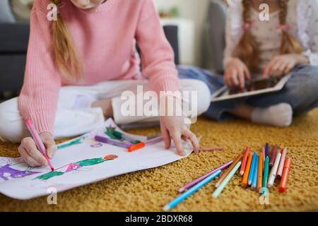 Gros plan de fille assise sur le sol et dessin avec des crayons de couleur avec sa sœur à la maison Banque D'Images