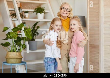Portrait de la grand-mère heureuse embrassant ses deux petites-filles et souriant à l'appareil photo tout en se tenant dans la chambre à la maison Banque D'Images