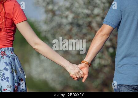 L'homme et la femme tiennent les mains sur le fond des jardins en fleurs. Banque D'Images