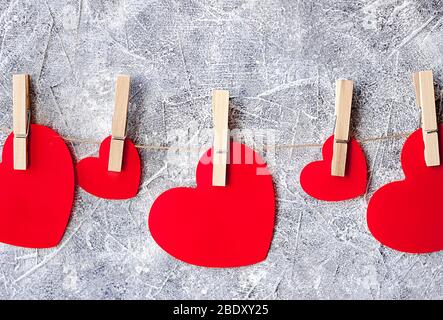 Coeurs en papier rouge accrochés sur la corde à ficelle en lin avec des tours sur fond de barriette et de mur blanc Banque D'Images