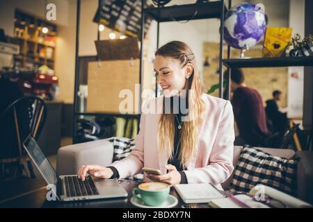 Belle jeune femme indépendante utilisant un ordinateur portable assis à la table Cafe. Femme d'affaires saisie de texte, utilisation de portable contact recherche d'affaires Banque D'Images