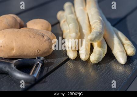 asperges blanches non pelées avec un éplucheur et des pommes de terre sur une table Banque D'Images