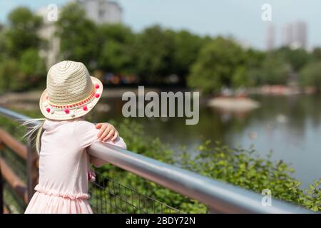 Une jeune fille portant un chapeau regardant le lac et les arbres dans un parc à l'extérieur. Vue arrière Banque D'Images