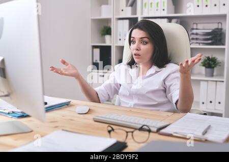 Jeune femme d'affaires surprise avec des mains tendues regardant l'écran d'ordinateur avec une expression perplexe tout en travaillant au bureau Banque D'Images