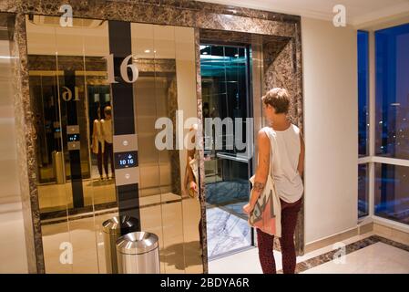 Blonde femme avec un sac à main avec des cheveux courts entrant dans un ascenseur la nuit Banque D'Images