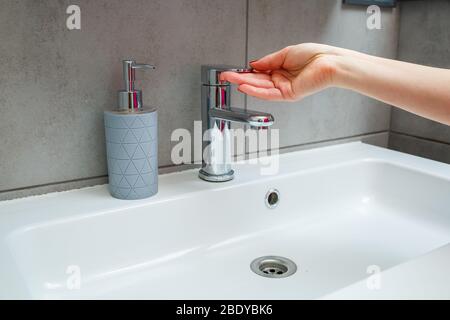 Lavabo blanc avec robinet en argent dans la salle de bains. CAN gris avec savon liquide pour les mains. Activation de l'eau du robinet, hygiène personnelle des mains Banque D'Images
