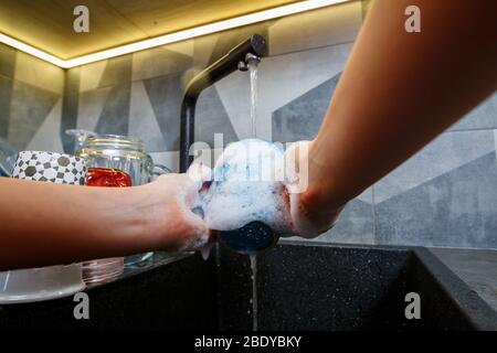 Mains avec éponge laver la tasse sous l'eau, femme de ménage dans le mug bleu dans un évier de cuisine avec une éponge bleue, nettoyage des mains, manuellement, housewo Banque D'Images