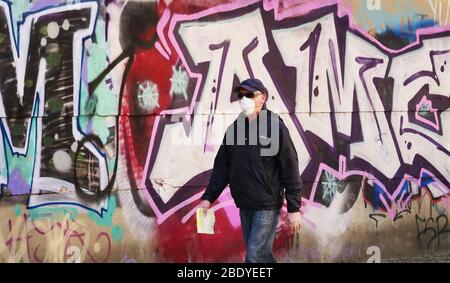 27 mars 2020, Berlin: Un homme âgé porte un masque respiratoire, des gants jetables et des lunettes de soleil pour se protéger contre le nouveau coronavirus lorsqu'il passe le graffiti après son passage à une pharmacie. Photo: Wolfram Steinberg/dpa Banque D'Images