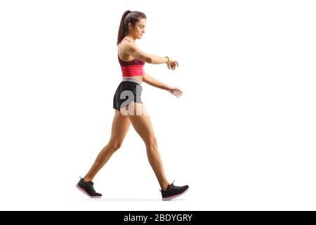 Photo pleine longueur d'une jeune femme en forme marchant en vérifiant son brassard de sport isolé sur fond blanc Banque D'Images