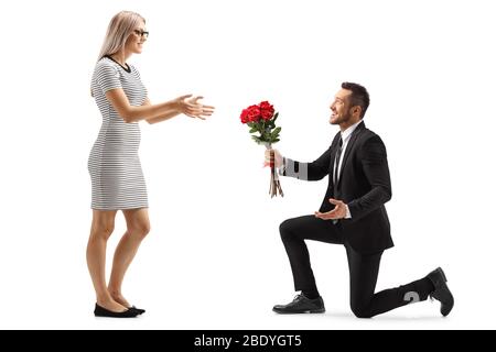 Jeune homme de handsome dans un costume à genoux et donnant un groupe de roses rouges à une femme isolée sur fond blanc Banque D'Images