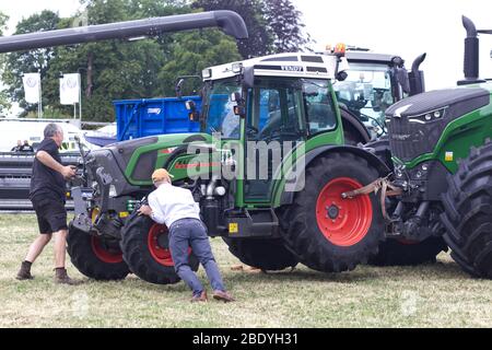 Les hommes poussant et tirant un tracteur Fendt en place qui est attaché à un autre tracteur Fendt. Banque D'Images