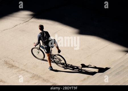 Belgrade, Serbie - 18 mars 2020: Jeune homme qui se met en vélo sur le trottoir de la rue de la ville devant les escaliers publics, une journée ensoleillée, arrière haute angle Banque D'Images