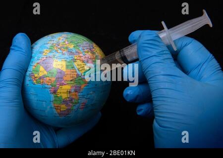 Un modèle de planète Terre tenu dans les mains portant des gants chirurgicaux bleus, également tenant une seringue hypodermique. Banque D'Images