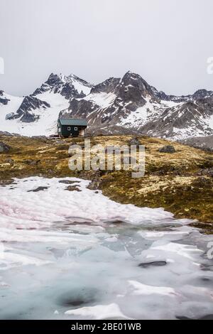 Petit bâtiment vert pour un abri dans l'arrière-pays sauvage de l'Alaska, en dessous d'un grand pic couvert de glaciers. Banque D'Images