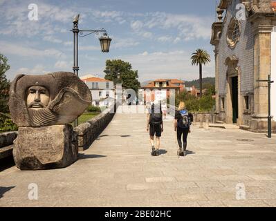 Deux randonneurs féminins sur la route centrale Camino Portugués qui marchent à travers avec une grande statue de bienvenue BOM Camino à Ponte de Lima dans le nord du Portugal Banque D'Images