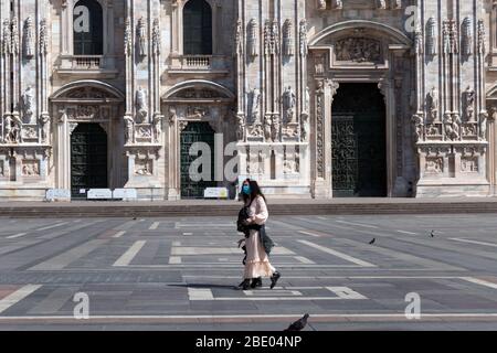 Vue sur une Piazza Duomo déserte à Milan, Italie pendant l'éclosion de COVID-19 avec la mère et la fille marchant. Ville de Milan et verrouillage du coronavirus Banque D'Images